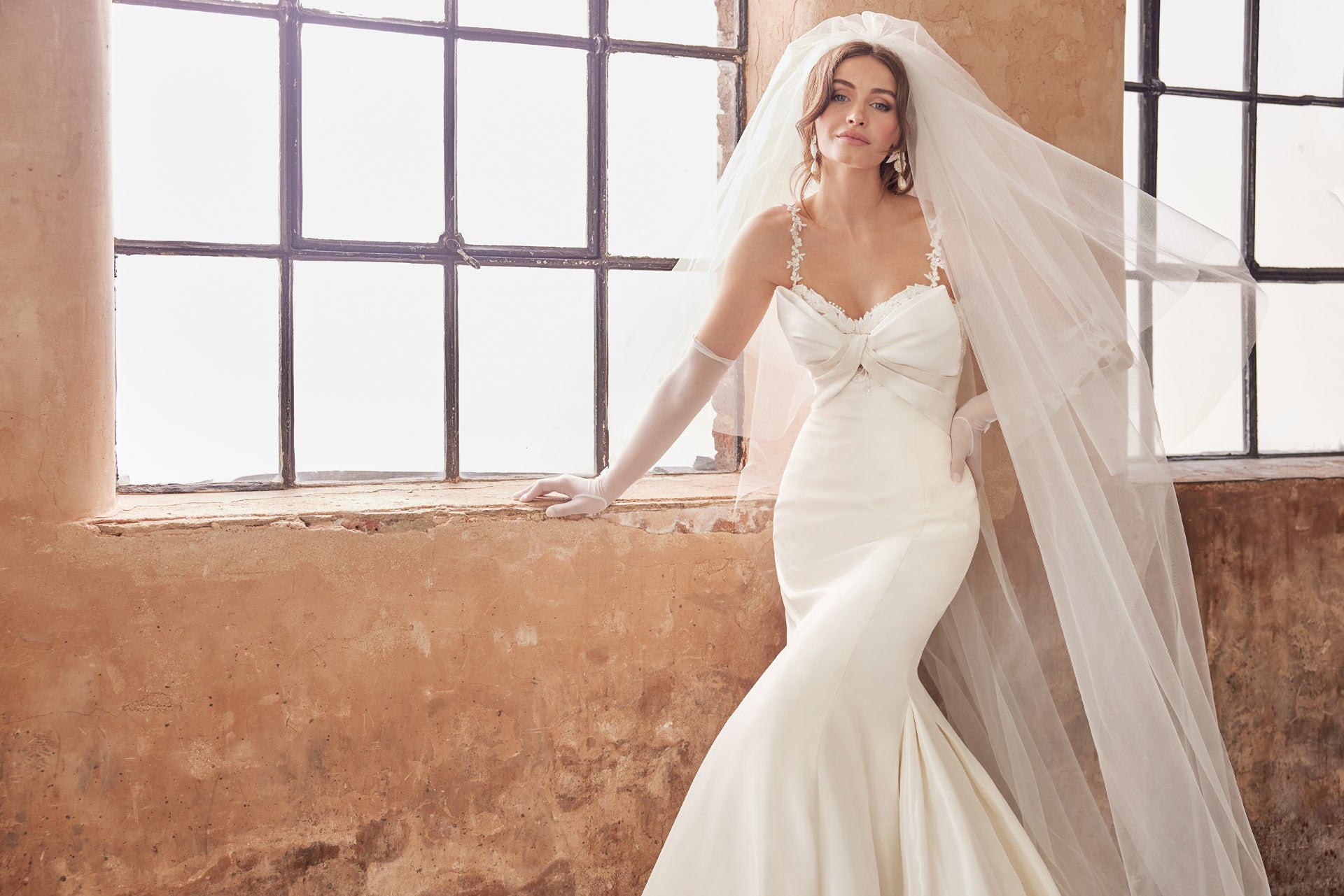 Fishtail silhouette of luxurious taffeta faced satin. Dramatic bow neckline and enviable fishtail silhouette, luxurious lace and back button detail along the train. Lace appliqued internal structured corset.