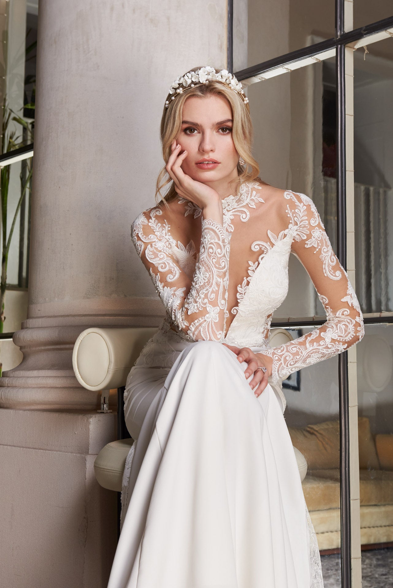 Crepe and lace fishtail gown with high-neck into elegant long lace sleeves. Dramatic illusion back with pearl buttons. Godets of lace embellished with lace appliqué flow into train.
