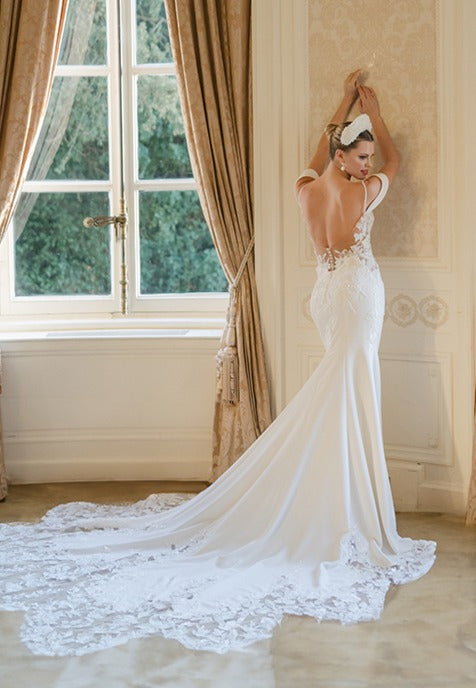 Elegant crepe sheath gown with 3D lace appliqué covered corset, detachable sleeves, delicate beaded straps and cowl back and dramatic floral lace cut-out train.