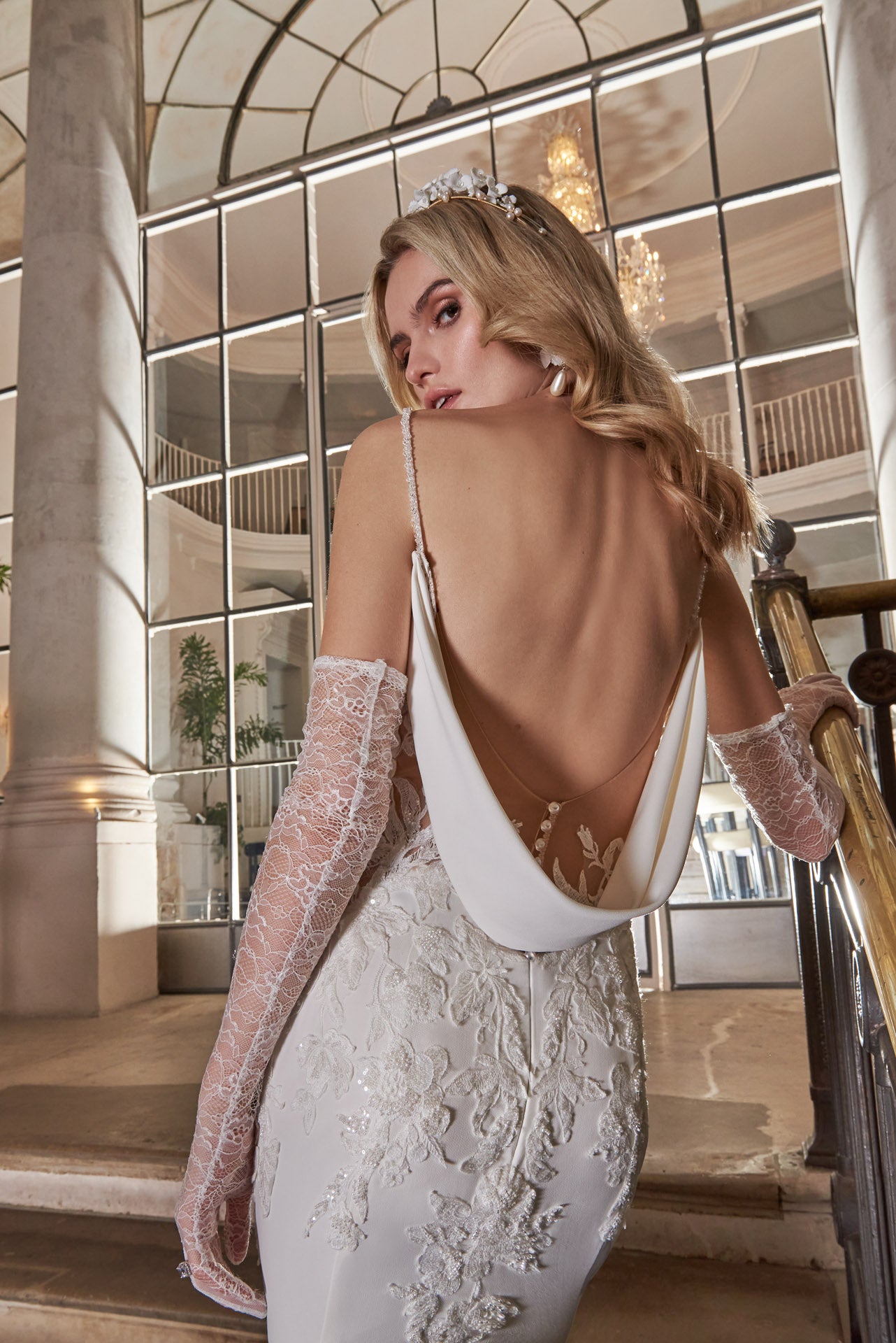 Elegant crepe sheath gown with 3D lace appliqué covered corset, detachable sleeves, delicate beaded straps and cowl back and dramatic floral lace cut-out train.