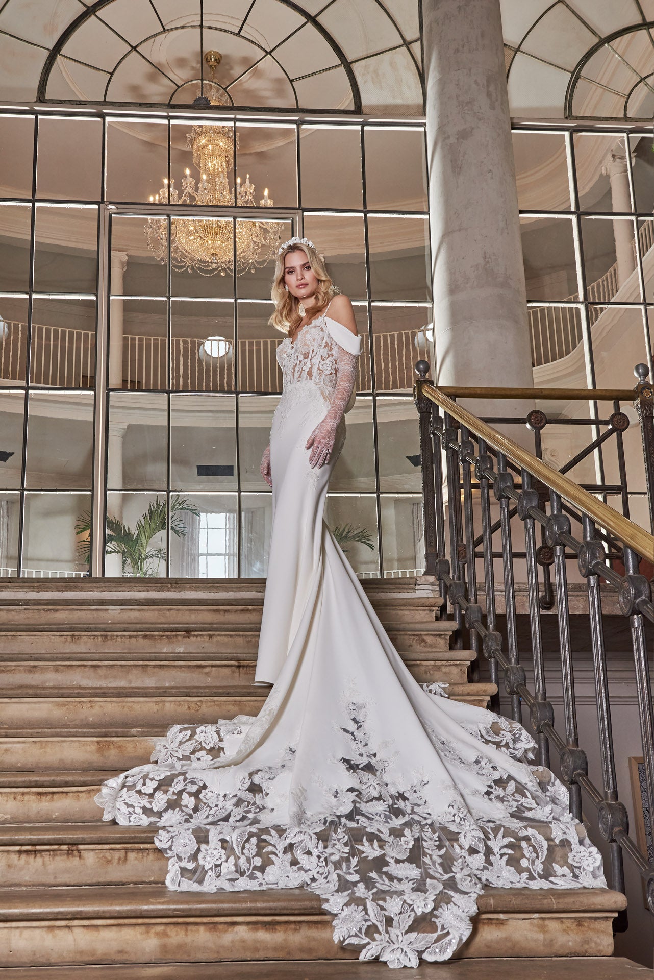 Elegant crepe sheath gown with 3D lace appliqué covered corset, detachable sleeves, delicate beaded straps and cowl back and dramatic floral lace cut-out train.