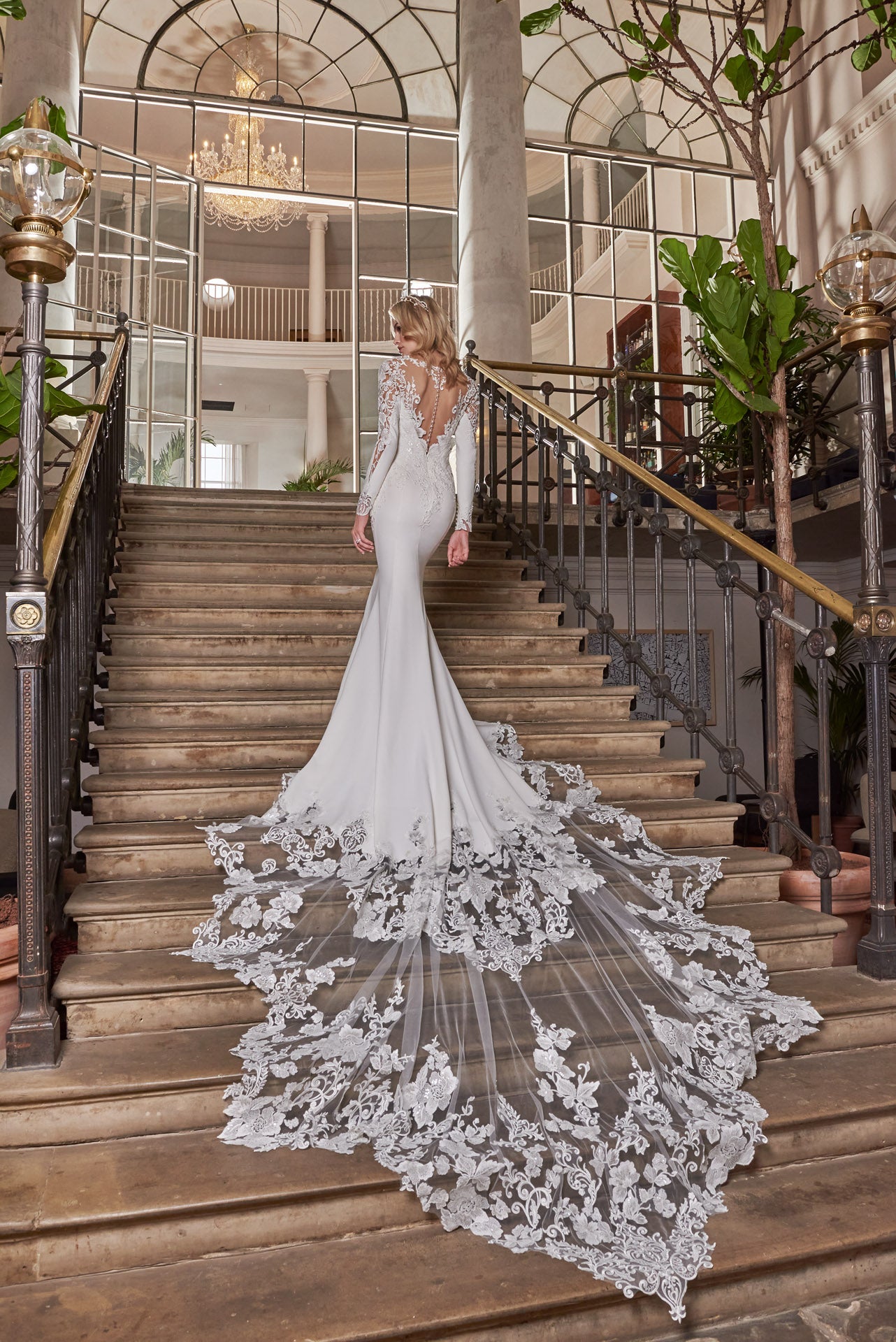 A luxury crepe sculpted dress, lace double tiered train with detailed lace appliqué. A timeless open v-neckline with cut-out sleeves with divine cuff detail. Illusion exposed back.