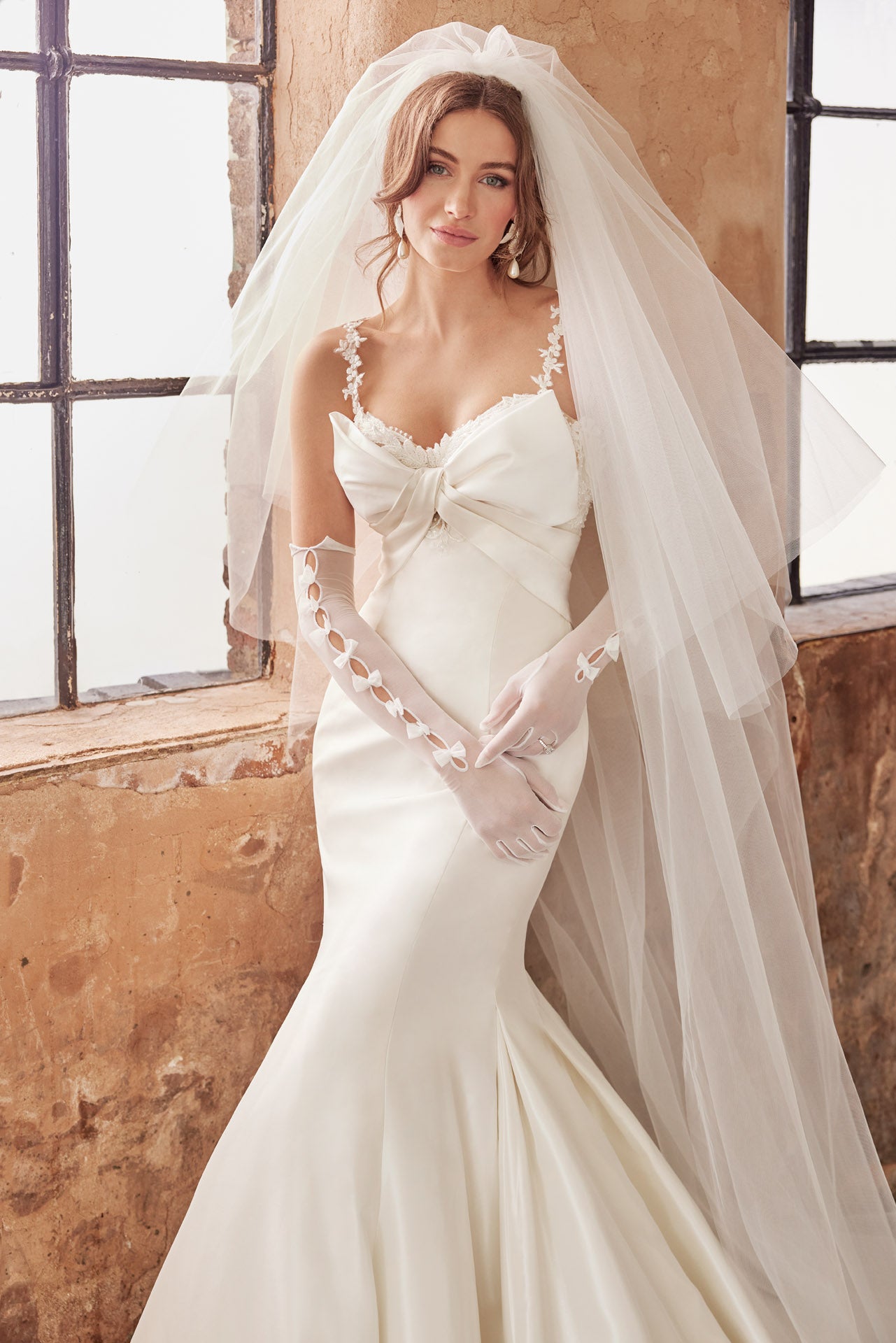 Fishtail silhouette of luxurious taffeta faced satin. Dramatic bow neckline and enviable fishtail silhouette, luxurious lace and back button detail along the train. Lace appliqued internal structured corset.