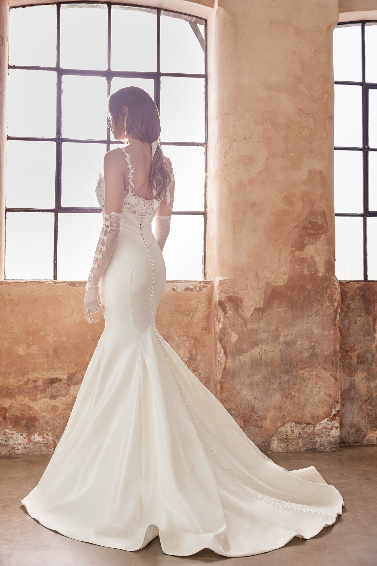 Fishtail silhouette of luxurious taffeta faced satin. Dramatic bow neckline and enviable fishtail silhouette, luxurious lace and back button detail along the train. Lace appliqued internal structured corset.