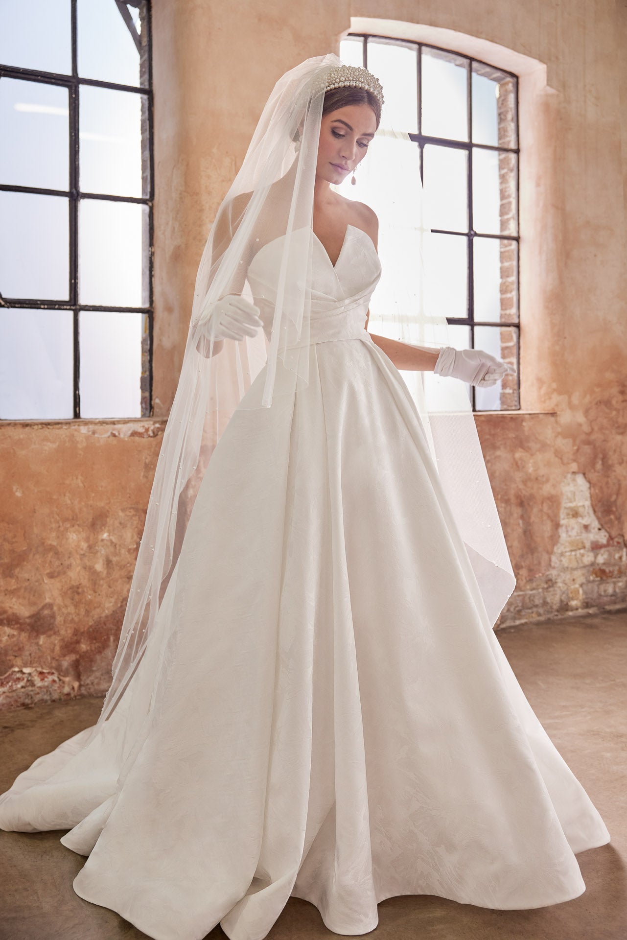 Embossed jacquard A-Line gown with strapless neckline and full skirt. Wrap around waist and pearl buttons along the back into the train.