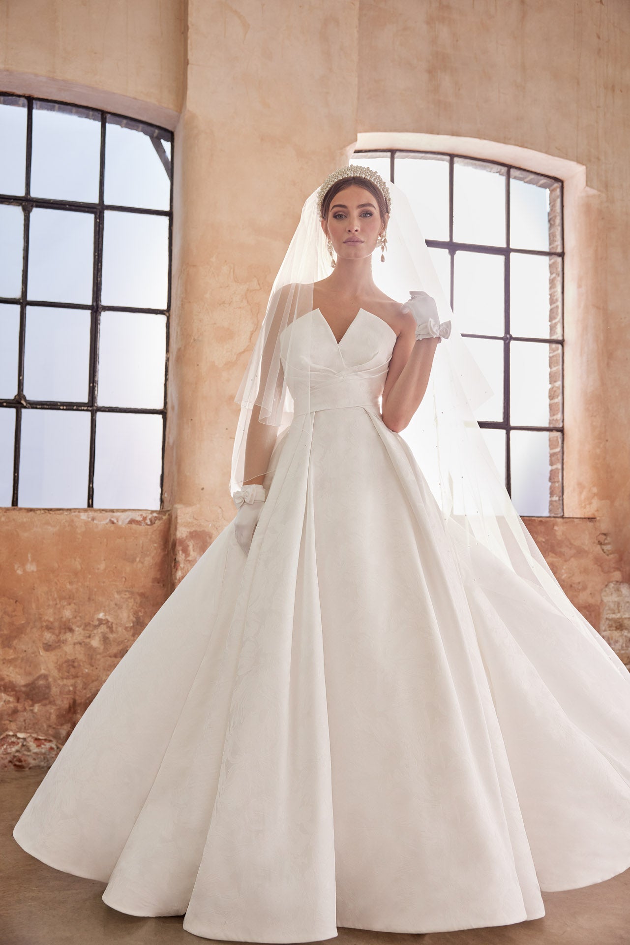 Embossed jacquard A-Line gown with strapless neckline and full skirt. Wrap around waist and pearl buttons along the back into the train.