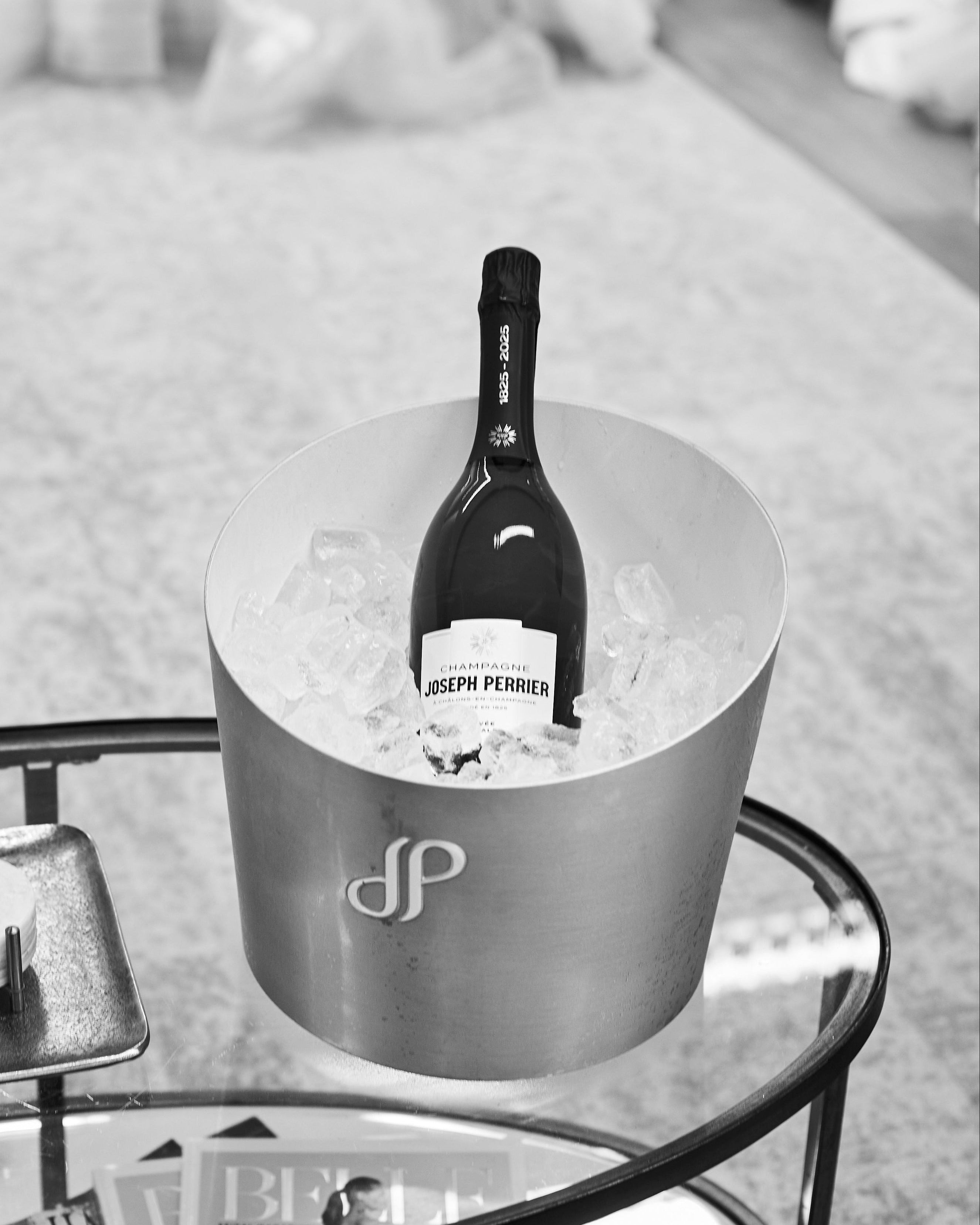 Bottle of Joseph Perrier champagne in an ice bucket on a glass table.