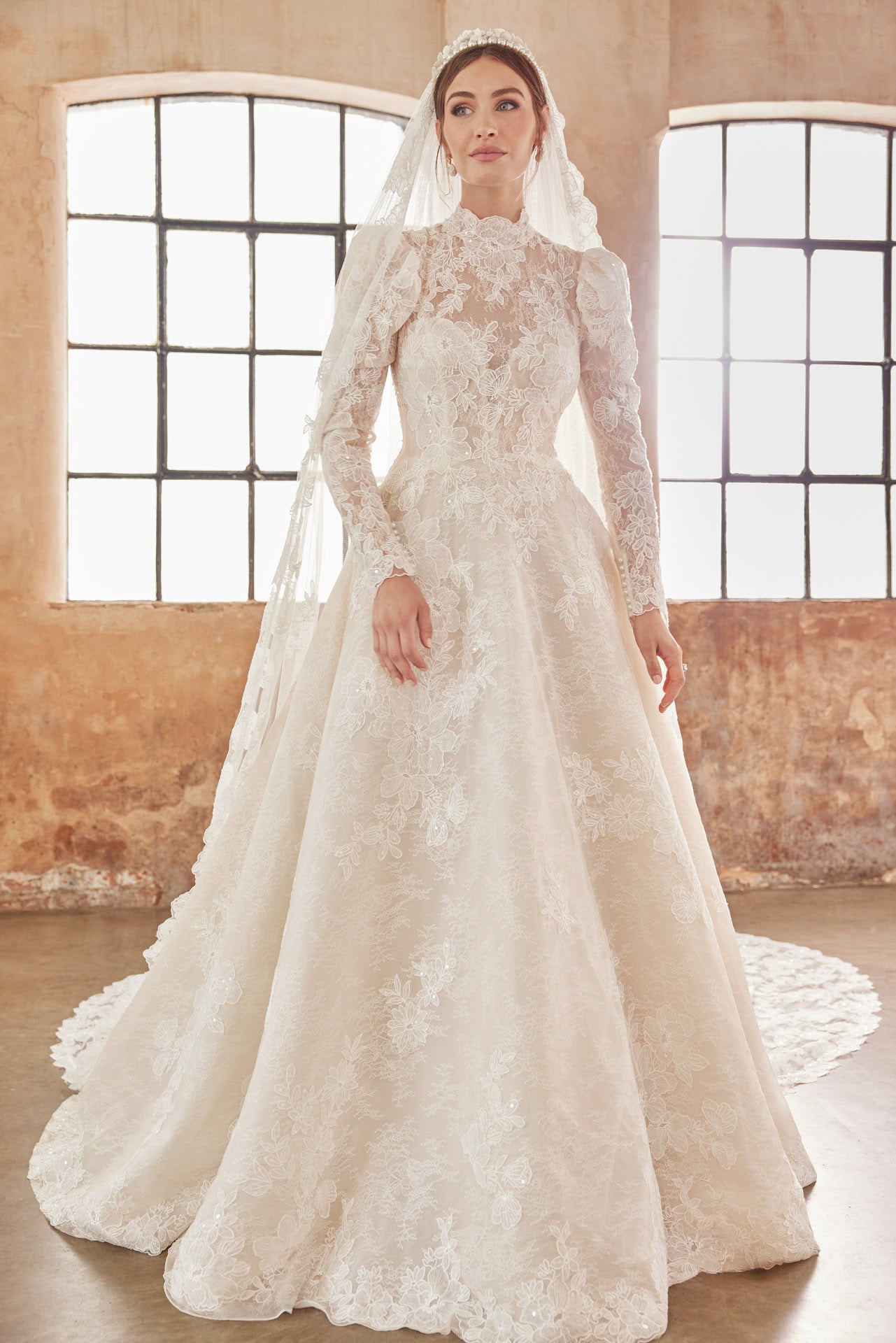 High-neck luxury lace A-line gown with romantic long puffed sleeves. Finest embroidered lace with a full skirt. Keyhole back and full length covered buttons on train.