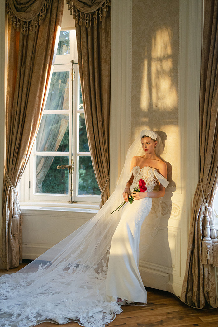 Elegant crepe sheath gown with 3D lace appliqué covered corset, detachable sleeves, delicate beaded straps and cowl back and dramatic floral lace cut-out train