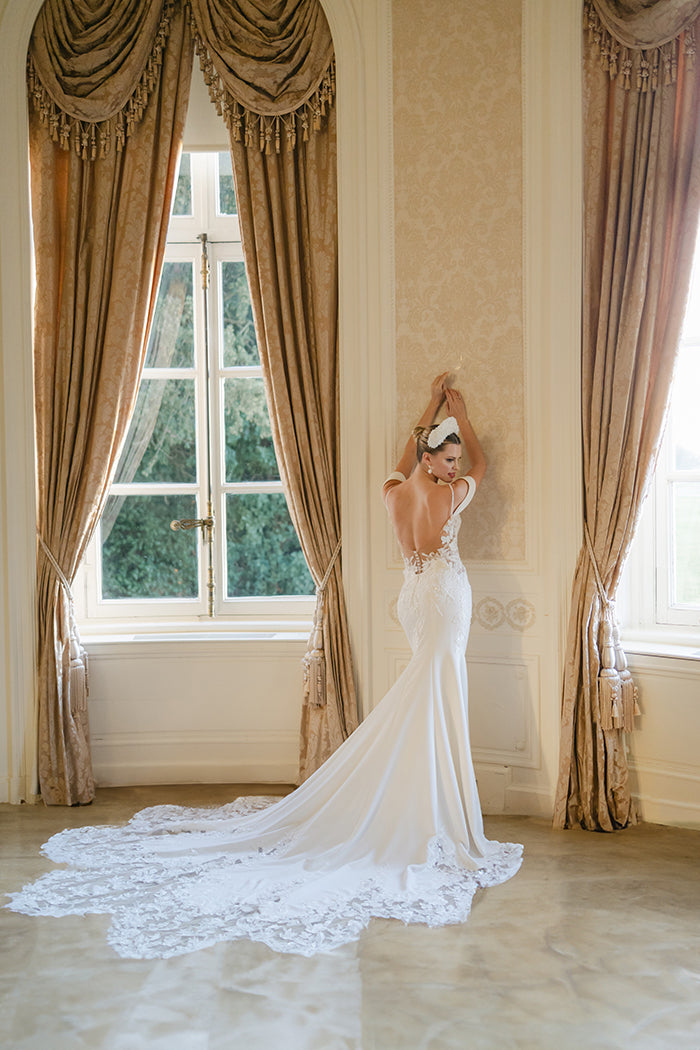 Elegant crepe sheath gown with 3D lace appliqué covered corset, detachable sleeves, delicate beaded straps and cowl back and floral lace cut-out dramatic train.