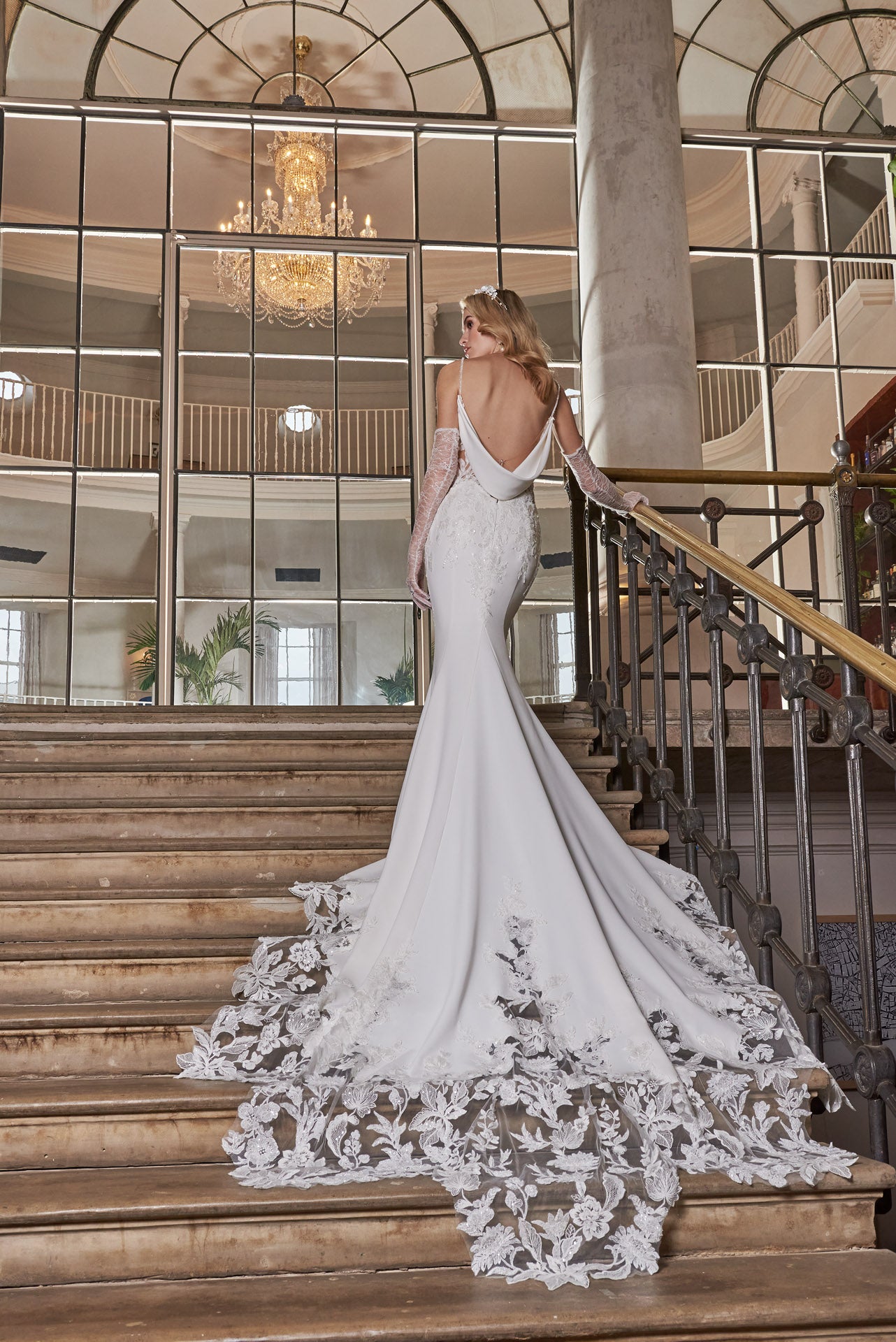 Elegant crepe sheath gown with 3D lace appliqué covered corset, detachable sleeves, delicate beaded straps and cowl back and dramatic floral lace cut-out train.